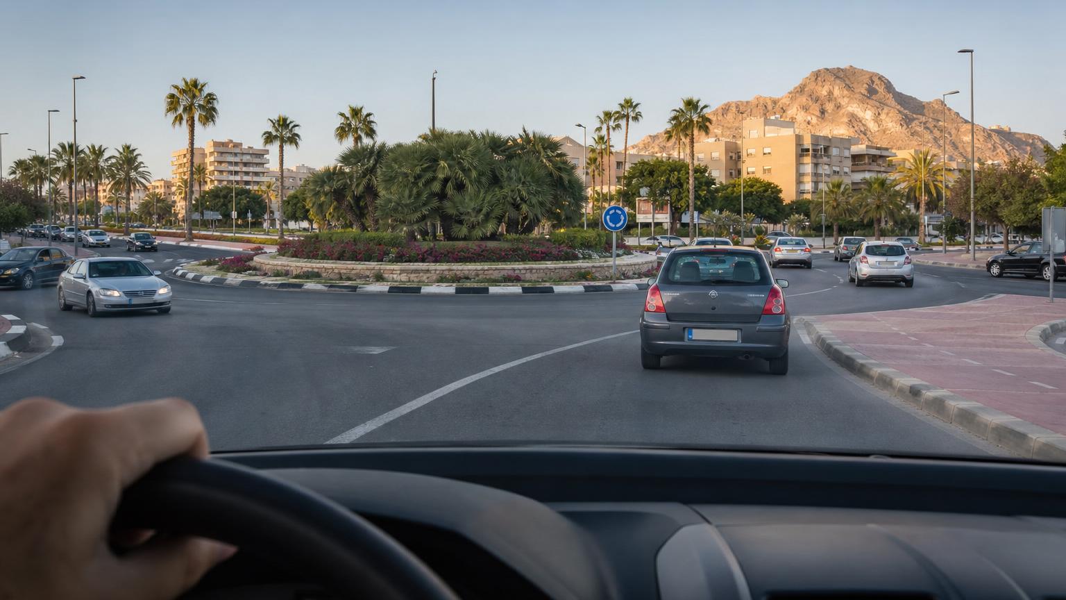Driver’s point-of-view of a multi-lane roundabout in Alicante with palm trees, city buildings, and a rocky mountain under a clear sky. Driver's point-of-view of a multi-lane roundabout in Alicante with palm trees, city buildings, and a rocky mountain under a clear sky.